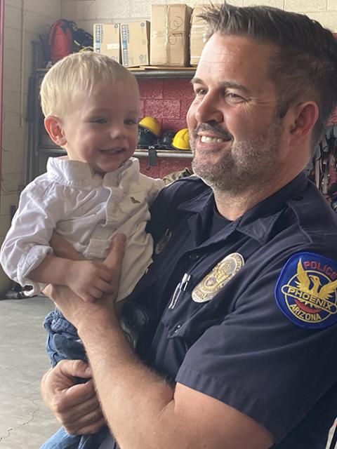 15-month old Vincent Robinson is carried in the arms of the Phoenix Police officer who first arrived at the Robinsons' home on the morning Vincent's father found him March 2 face-down at the bottom of the family's hot tub that was not turned on, in Phoenix March 26, 2025. (OSV News/Courtesy of Phoenix Fire Department)