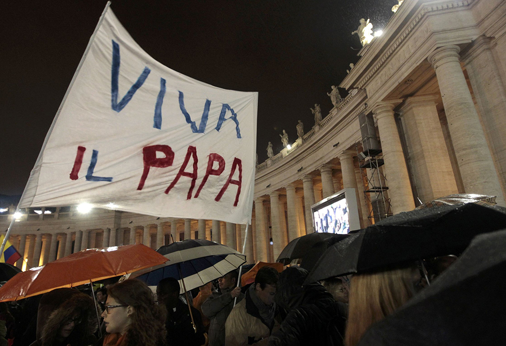Pilgrims wave a banner saying "Viva il papa" ("Long live the pope") as white smoke rises from the chimney above the Sistine Chapel, indicating a new pope has been elected at the Vatican, in this photo from March 13, 2013. The conclave to elect a new pope met over two days before making a decision. (CNS/Reuters/Giampiero Sposito)